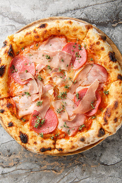 neapolitan meat pizza with prosciutto salami herbs close-up on a wooden board. Vertical top view