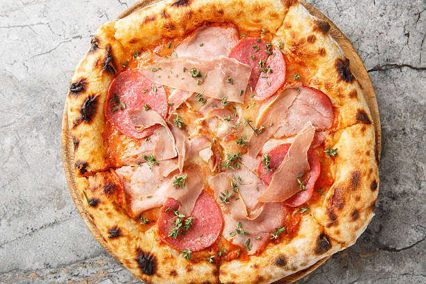 Charred meat pizza with prosciutto, salami, bacon and ham close-up on a wooden board. Horizontal top view