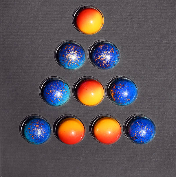 10 chocolate colored ball pralines. Colorful handmade pralines arranged in a pyramid pattern on a dark background.