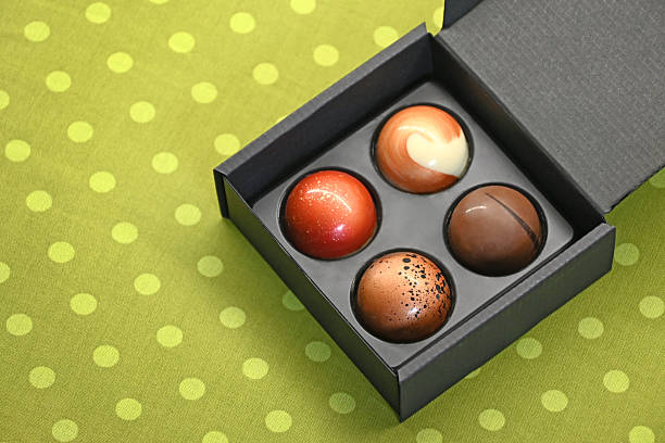 Chocolate pralines. 4 colorful round sweet chocolate candies in a black square box and on a green dotted background.