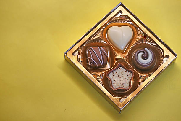 4 different shaped sweet chocolate candies in a square gift box and on a yellow background. Chocolate pralines.