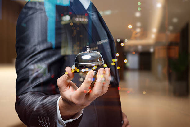 A well-dressed man holds a silver service bell in a luxurious hotel lobby.
