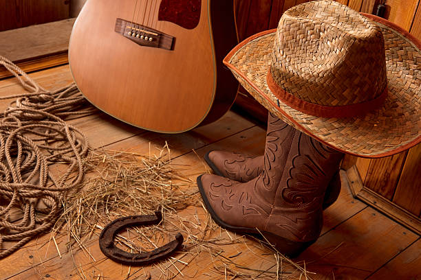 Acoustic guitar, rope, old rusty horseshoe, cowboy hat and boots on a barn wood texture background. American Country music concept.