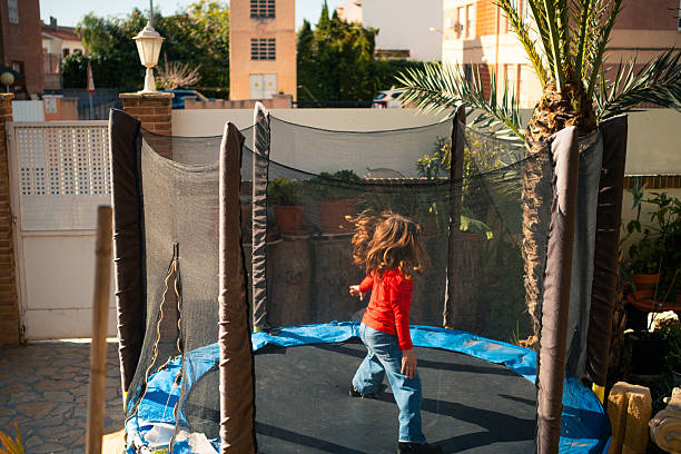 Young girl with long brown hair jumping on a trampoline in a backyard