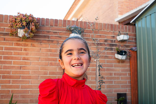 Happy elementary age girl laughing while standing outdoors in front of a brick wall