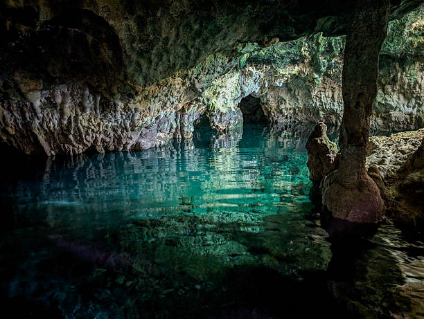 Maalum Cave's transparent turquoise pool flows through ancient limestone grotto, calm surface mirroring rock formations for a tranquil, secluded underground sanctuary of natural beauty