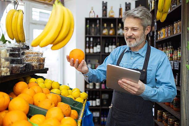 Grocer holding orange and digital tablet in grocery store