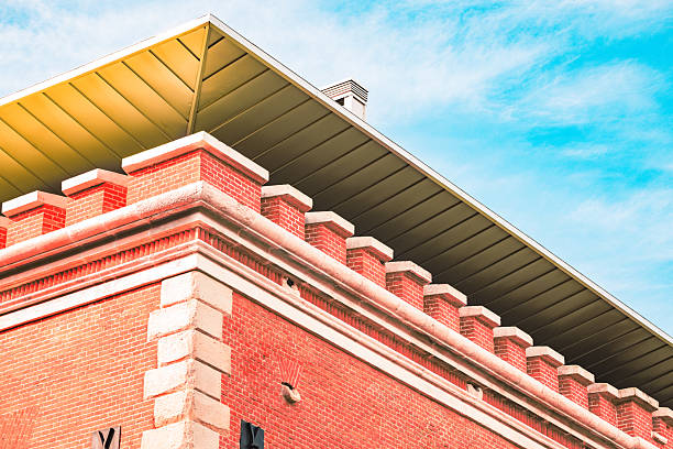 A striking contrast between old and new architecture, featuring a red brick structure with a modern yellow roof extension against a vibrant blue sky