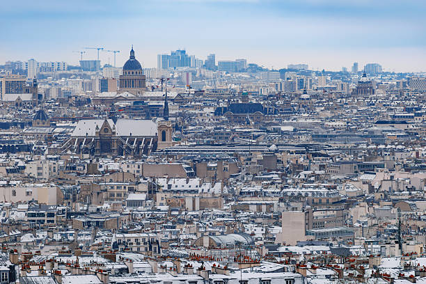 A panoramic view of Paris showcases snow-covered rooftops, dome of Pantheon, a cloudy sky, emphasizing the unique architecture and winter atmosphere of this beautiful city