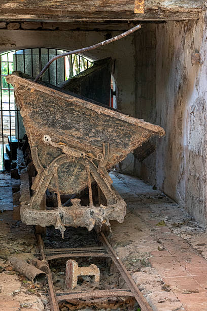 Mexico - Temozon - Hacienda Temozon Sur - a rusted iron cart sits abandoned on its rails inside the crumbling stone factory building, a poignant remnant of the industrial machinery that once drove this estate's prosperity. The peeling walls, broken roof timbers and encroaching light from above create a compelling atmosphere of industrial archaeology, telling the story of the Yucatan's henequen era in an evocative language of rust, decaying stone and eloquent silence.