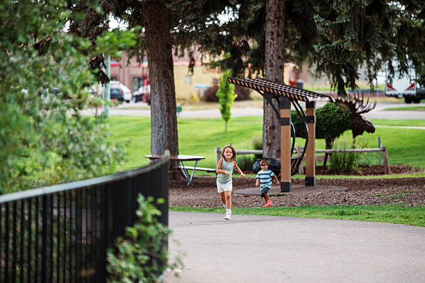 A brother and sister run freely along a scenic riverside trail while sightseeing in Idaho Falls, Idaho during a family road trip, capturing the joy of childhood and outdoor family recreation.