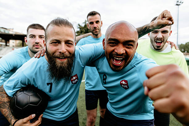 Soccer players lifting a teammate on their shoulders after scoring a goal. Football players screaming in joy pumping their fists in excitement celebrating victory.