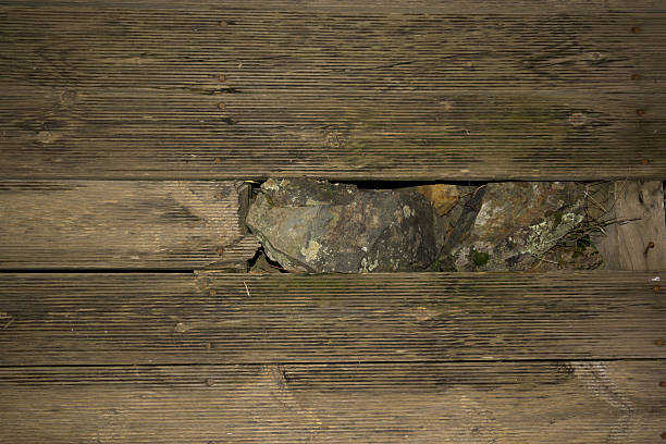 Top view of weathered wooden planks with visible gap revealing stones beneath rustic texture background for design and construction concepts