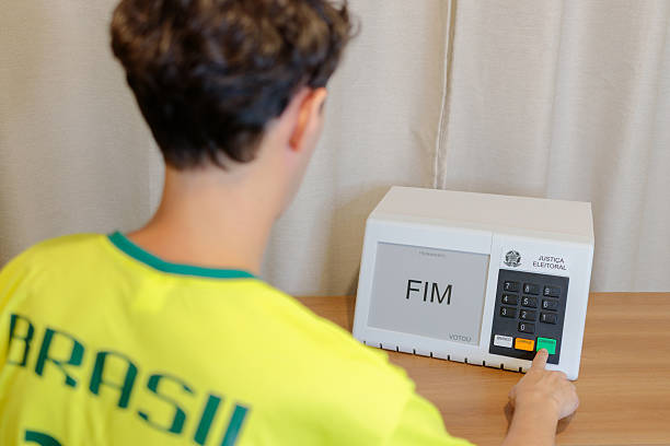 Brazilian man wearing a Brazil shirt casting a vote on an electronic ballot box, with the man intentionally blurred while the ballot box remains in sharp focus. The screen displays the word “End,” indicating the vote has been completed. Concept of Brazilian presidential elections, democracy, civic duty, digital voting, and political participation.