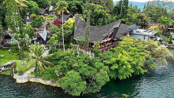 Samosir Islands, Indonesia, September 9, 2025. Cluster of traditional Batak longhouses on Samosir, Sumatra, enveloped in palms and lush greenery above deep blue waters.