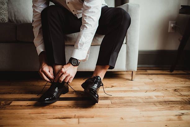 Groom getting dressed for wedding ceremony tying black dress shoes