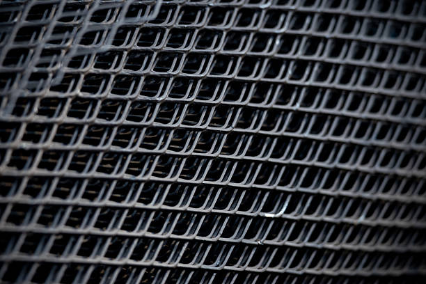 A close up of a black metal mesh with a black background. The mesh is made of metal and has a grid pattern