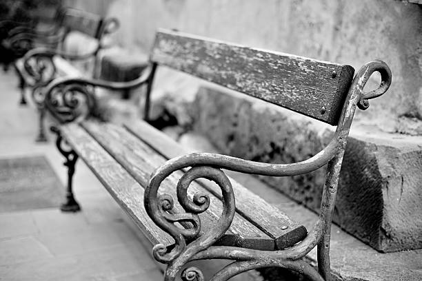 Black-and-white close-up of ornate wrought-iron and wooden park benches aligned along a stone wall, weathered textures and shallow depth of field