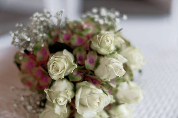 Shot during a wedding procession, this image shows the bride and bridesmaids holding tightly arranged pink rose bouquets. The shallow focus highlights the flowers against a blurred background of guests and ambiance lighting.