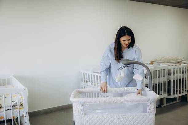 Young woman carefully setting up an infant bassinet, preparing for motherhood in a shop selling baby furniture