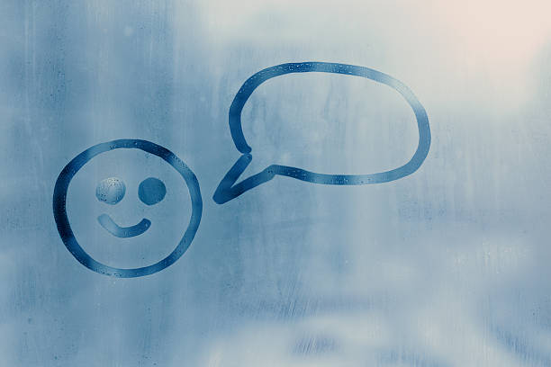Hand drawn doodle simple smiley face and empty speech bubble on misted glass blue window covered in condensation