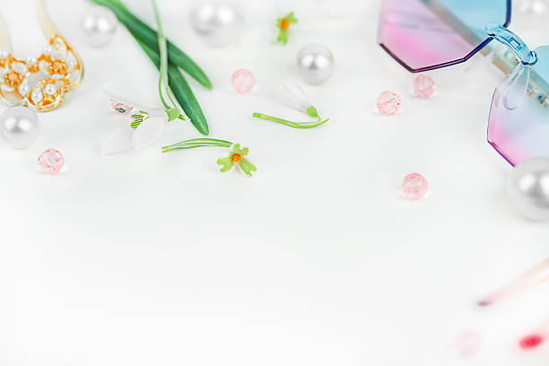 High-key spring flat lay composition with delicate snowdrop flowers, pastel fashion sunglasses, pearl-like beads, and pink decorative accents on a clean white background. Feminine seasonal beauty background with large copy space, ideal for greeting cards, social media banners, branding, and spring promotions.