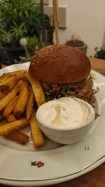 Delicious gourmet burger with sesame seed bun, crispy golden fries, and creamy dipping sauce served on elegant plate in outdoor dining setting