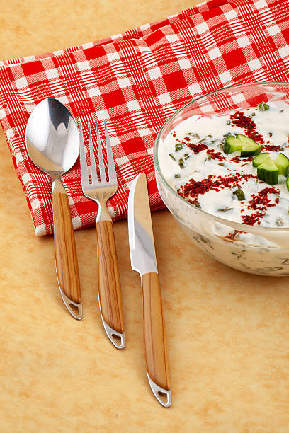 Cacik with chopped cucumber and red pepper flakes in a clear glass bowl, top view, natural light, centered composition.