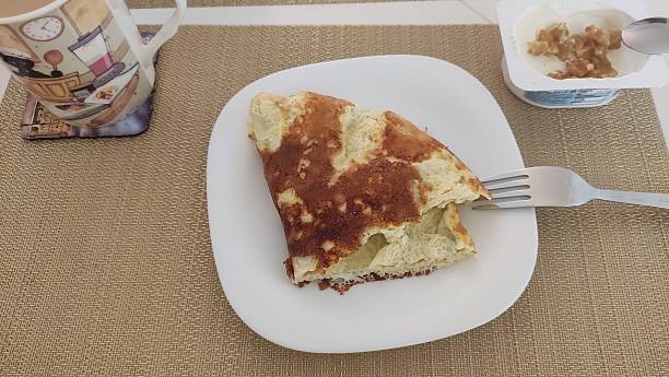 Folded omelette served on white plate for breakfast with coffee and yogurt