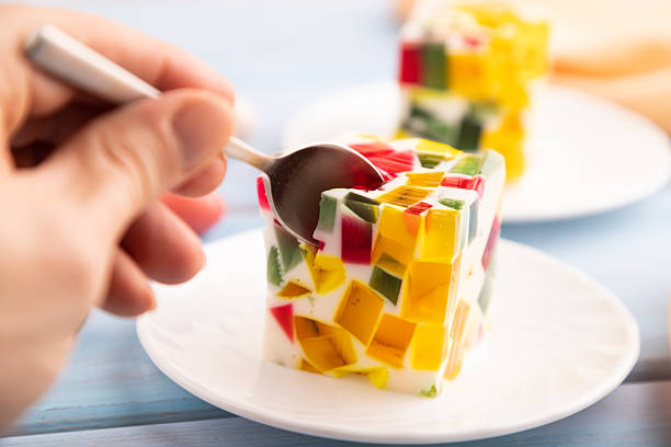 Colored Fruit and milk jelly with hand on blue wooden background and orange linen textile, side view, close up, selective focus