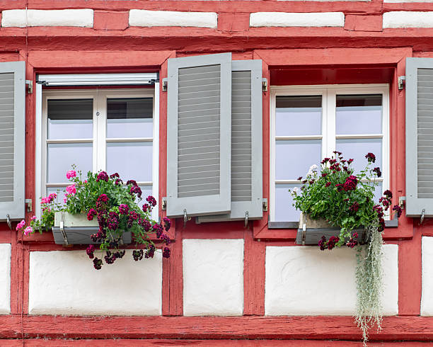 Three windows with open shutters and colorful flowers decorate a historic building in Stein am Rhein, Switzerland. The timber framing and floral accents highlight the charm of this Swiss town.