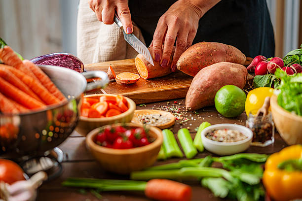 Unrecognizable person slicing fresh organic sweet potato in the kitchen. Woman preparing root vegetables for a vegetarian meal. Healthy eating or dieting for wellbeing