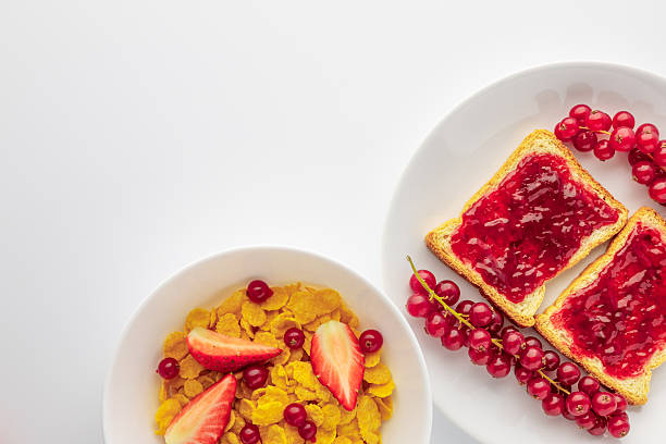 Breakfast includes cereal with strawberries and toast with jam arranged on a clean white table with empty space