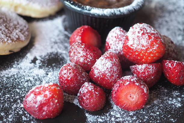 Juicy strawberries sprinkled with powdered sugar beside dessert bowl.