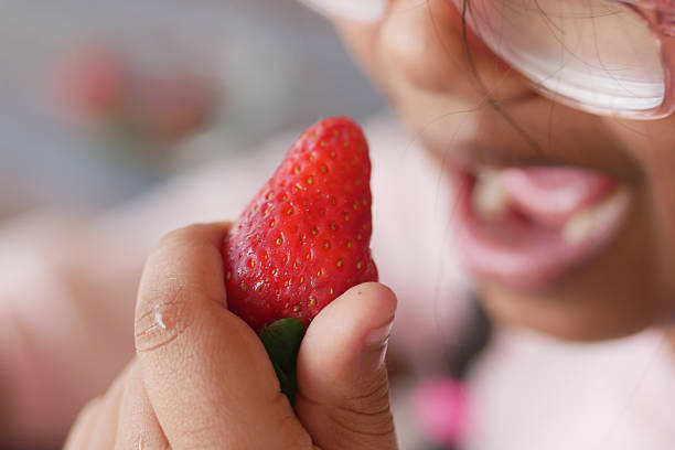 A young child holds a bright strawberry, smiling in delight while eating.