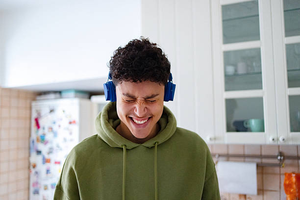 Happy boy with headphones is using digital tablet for listening to music and dancing at the public park. Enjoyment in nature after school.