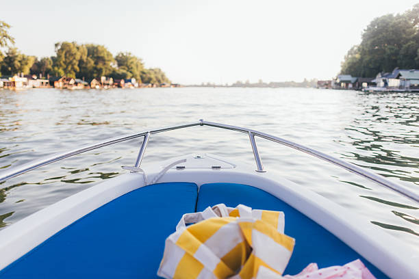 Bow perspective from a small boat cruising a calm lake near cottages on a sunny summer afternoon.