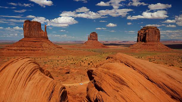 A stunning view of Monument Valley featuring iconic sandstone buttes under a bright blue sky with fluffy clouds.