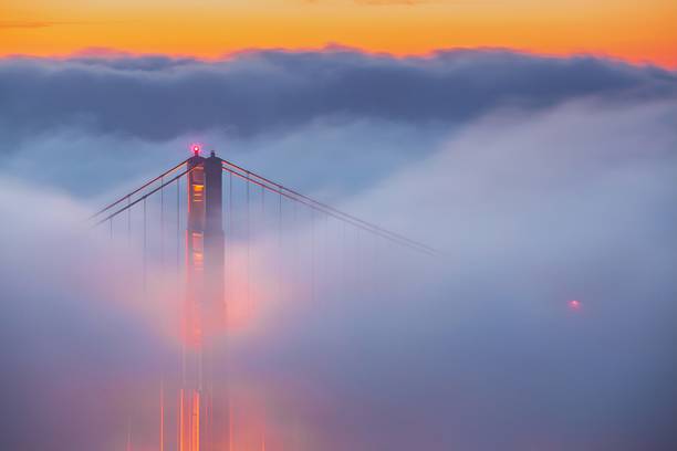 The Golden Gate Bridge emerging from fog at sunset, creating a dramatic and ethereal scene.