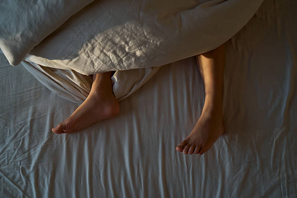 Person relaxing in bed, bare feet visible under a soft duvet, enjoying the peaceful morning light through a window