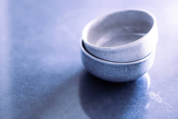 Two handcrafted ceramic bowls stacked on a cool-toned blue stone countertop, captured in soft natural light with a clean, minimalist aesthetic. Modern kitchen styling with subtle texture and gentle shadows, ideal for home decor concepts, Scandinavian interior design, tableware branding, culinary presentation backgrounds, product mockups, lifestyle blogs, restaurant marketing, contemporary dining visuals, copy space composition, and neutral kitchen styling themes.