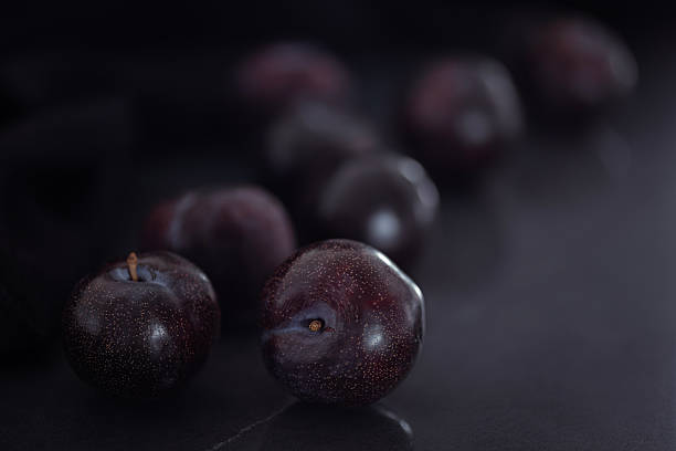 Ripe Red Plums on Dark Surface with Dramatic Low Key Lighting