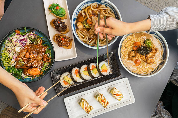 Hands reaching for Sushi Rolls and Noodle bowls.