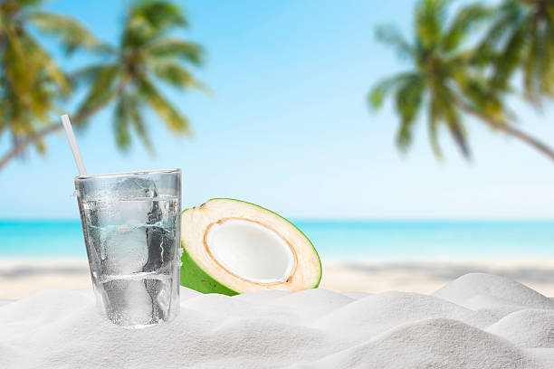Cold Coconut Water With Ice Cubes in Glass on Tropical Beach with Palm Leaves and Ocean Background