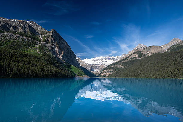 A breathtaking view of Lake Louise in Banff National Park, Alberta, Canada. The iconic turquoise waters are surrounded by the rugged peaks of the Canadian Rockies and dense evergreen forests. A world-famous travel destination symbolizing Canada travel, adventure, and pristine mountain landscapes. Perfect for themes of exploration, nature, road trips, and iconic scenic destinations.