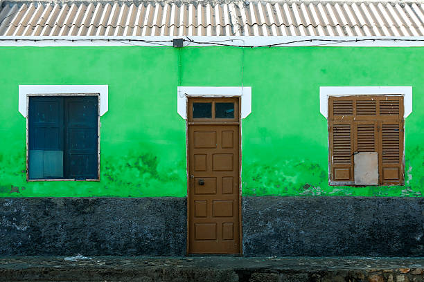 A small building with bright green walls, a central door, and windows with worn shutters. The vibrant colors and signs of wear are ideal for themes of architecture, urbanity, and visual authenticity.