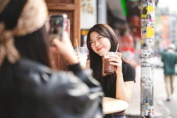 Two young asian woman gen z sisters using smartphone take photo. Influencer blogger at outdoor cafe share lifestyle travel moment on social media. Hipster sisterhood weekend tourism in Bangkok