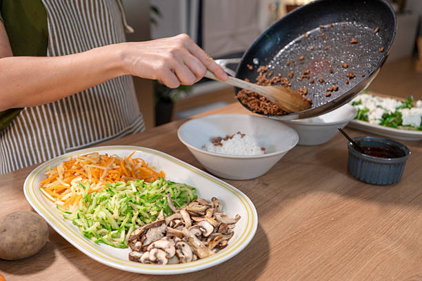 Person adding cooked ground meat to rice bowl with vegetables, preparing healthy dinner