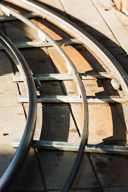 Curved metal track for a camera dolly system rests on the ground. Parallel rails and supporting crossbars are visible