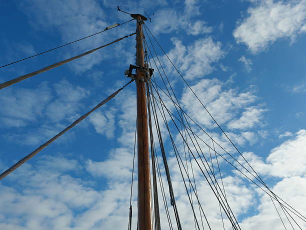 Sailing boat mast with rigging and diagonal ropes against blue sky with clouds. Copyspace